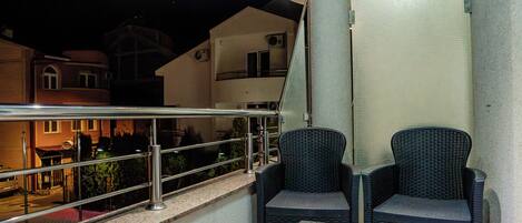 A balcony with two wicker chairs, a small table, and a railing.