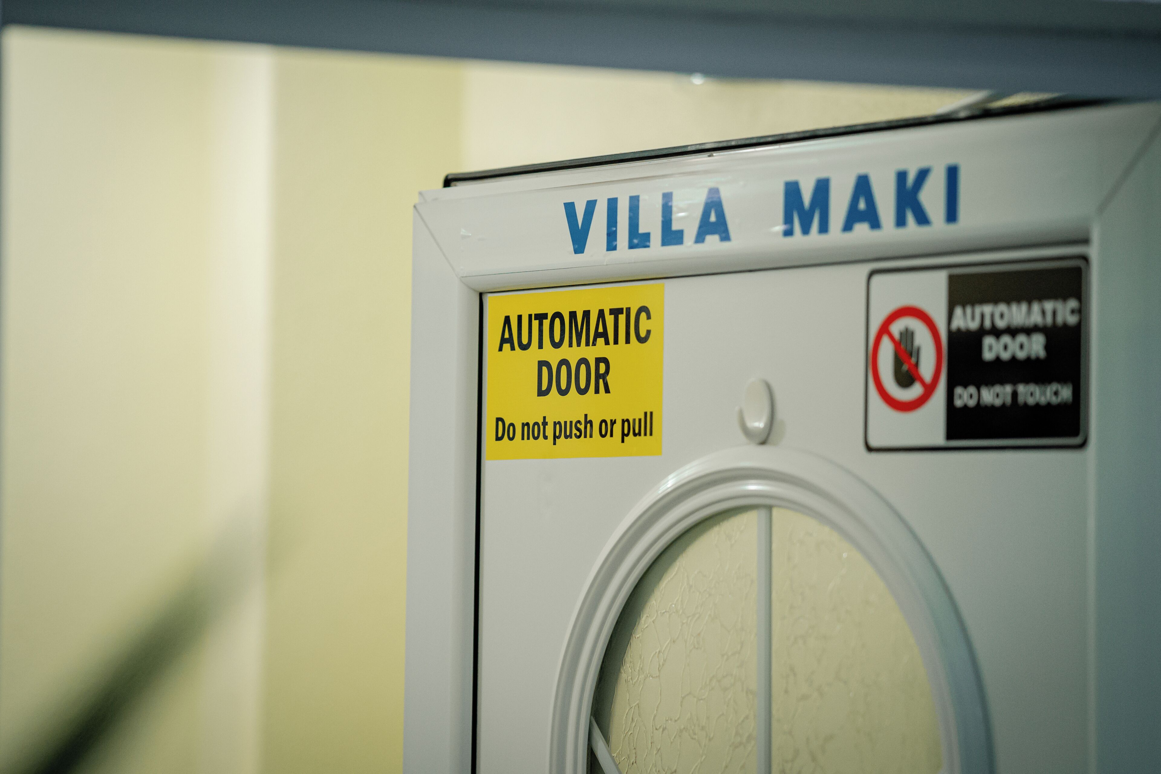 Una lavadora blanca con la marca 'VILLA MAKI' y dos etiquetas de advertencia: 'PUERTA AUTOMÁTICA No empujar ni tirar' y 'PUERTA AUTOMÁTICA NO TOCAR'.