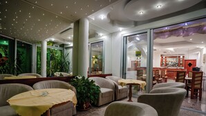 Um hall de hotel moderno com áreas de estar, um bar e um espaço de refeições envidraçado.