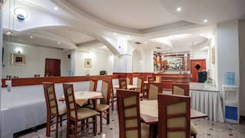 A restaurant with wooden chairs and tables, a counter with a display, and a water dispenser.