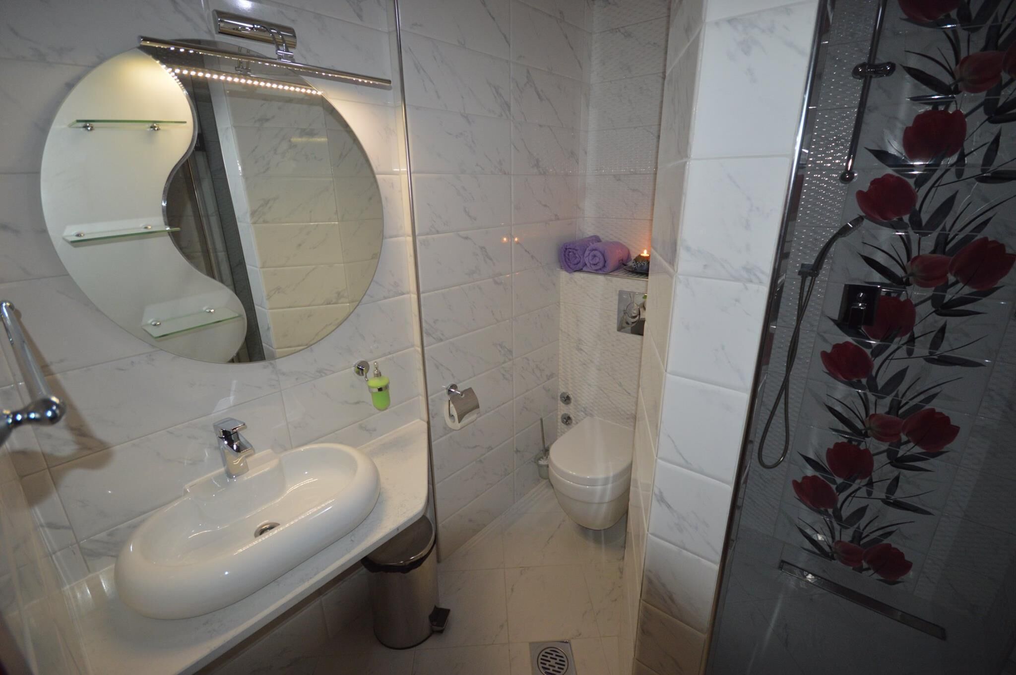 A bathroom with a white sink, a mirror, a toilet, and a shower with floral glass panels.