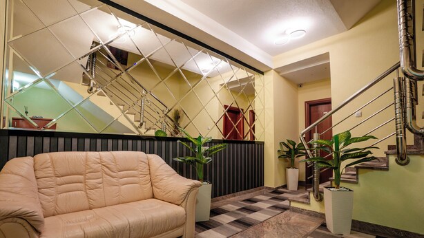 Un hall de hotel con piso a cuadros, un sofá color beige, plantas en macetas, una escalera y una barandilla de metal.
