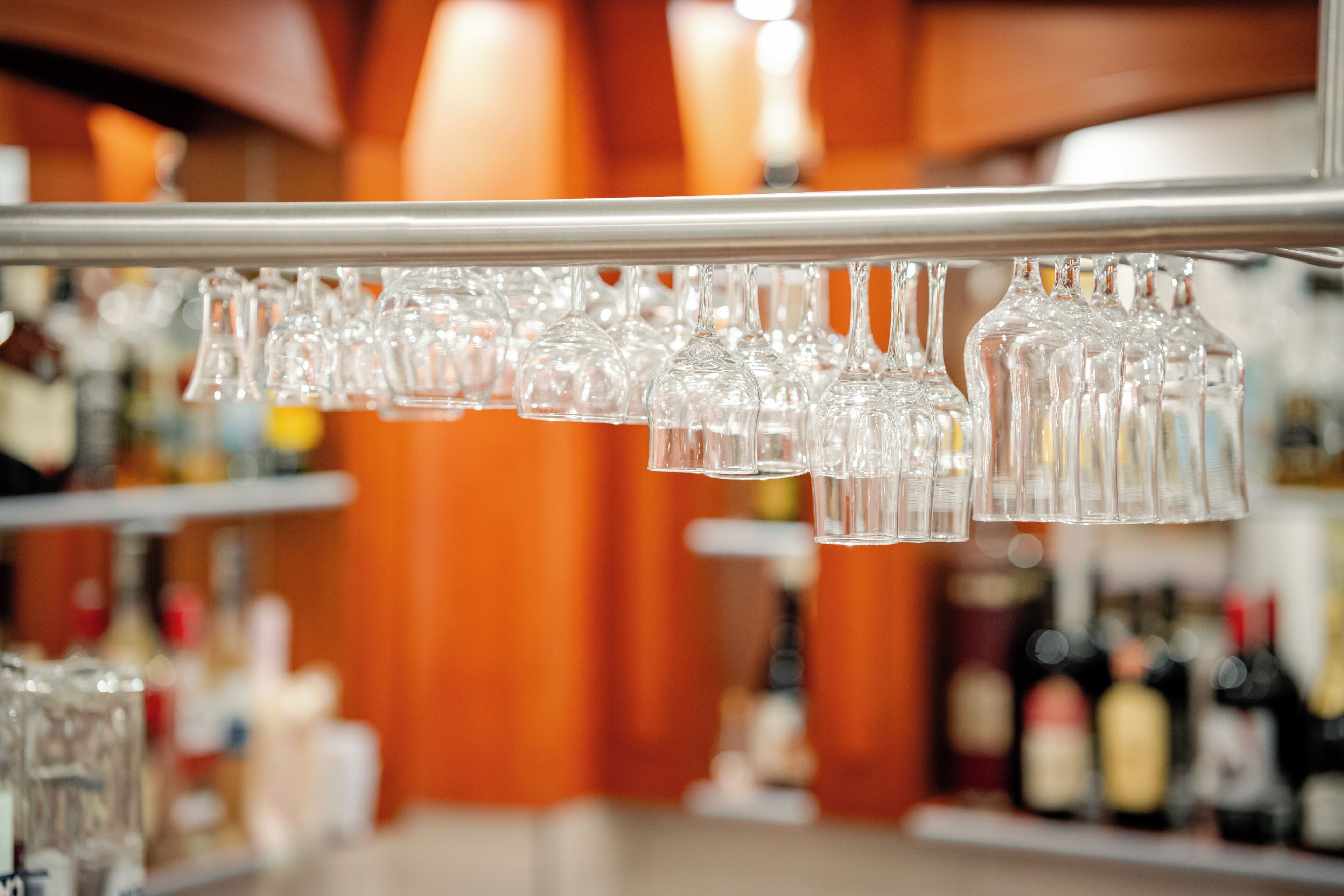 A bar area with a row of empty glasses hanging from a metal bar.