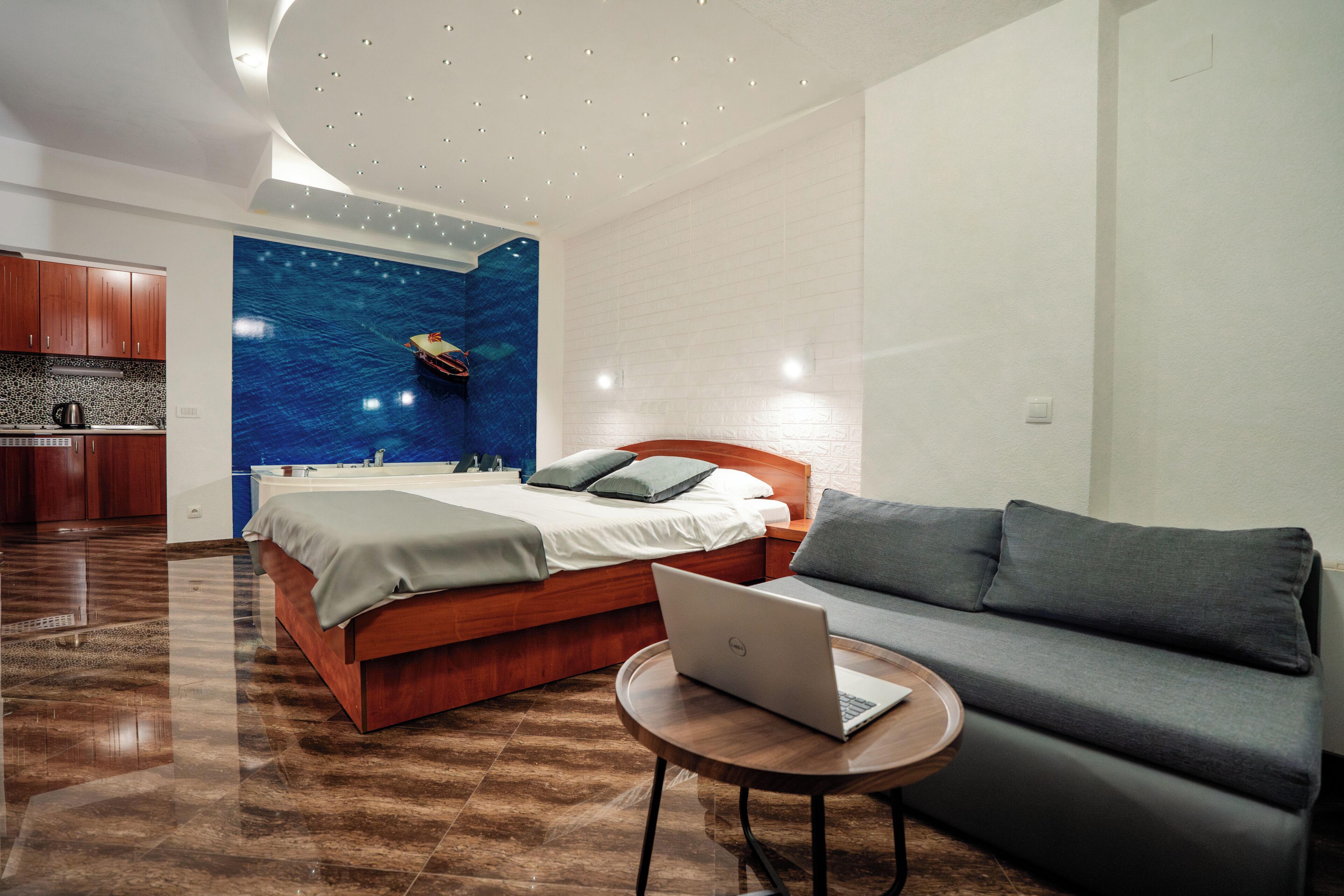 A modern hotel room with a bed, a sofa, a laptop on a small table, and a wall mural.