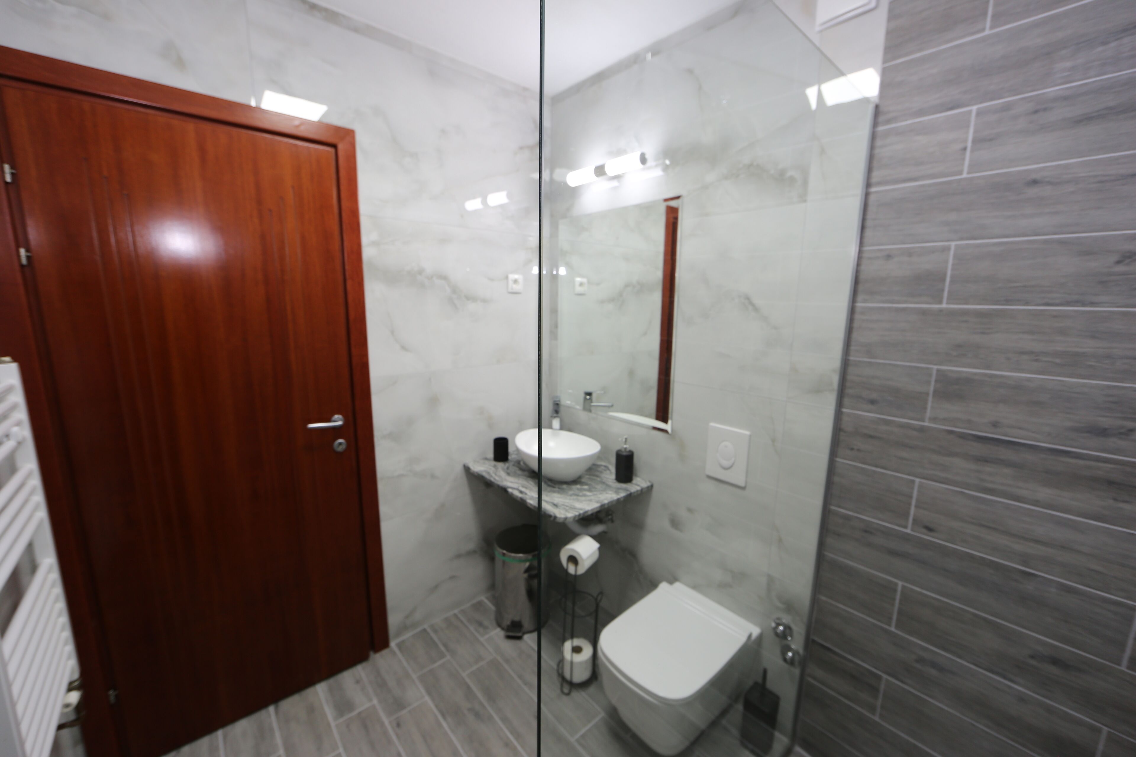 A modern bathroom with a wooden door, marble sink, and a toilet.
