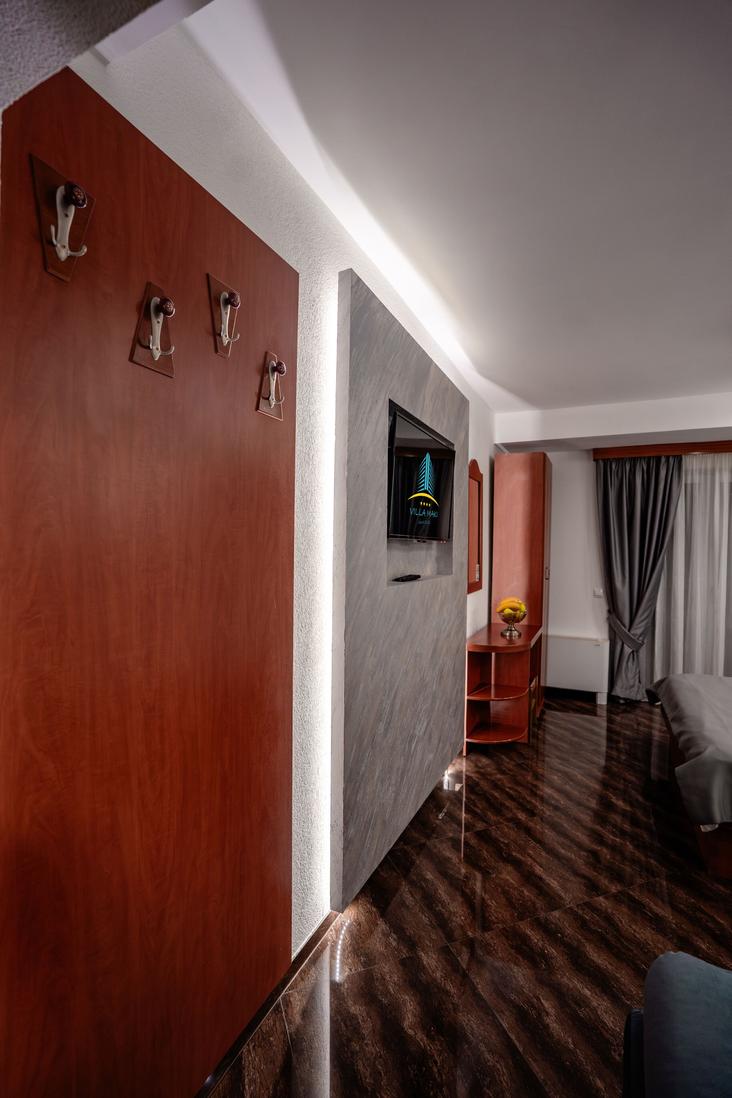 Een hotelkamer met een houten deur, een flatscreen televisie, een bed, een kleine tafel met een vaas en een raam met gordijnen.
