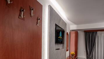 Quarto de hotel com porta de madeira, televisão de tela plana, cama, mesinha com um vaso e janela com cortinas.