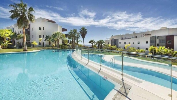 A swimming pool with clear blue water, surrounded by palm trees and modern buildings. - Hoyo19 11 | Premier Luxury Holiday Resort (Málaga)