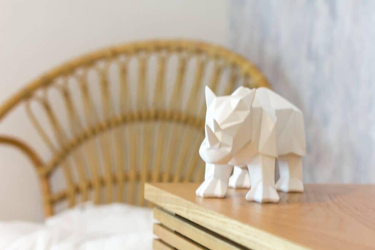 A white cat figurine on a wooden table in a room with a wicker chair.