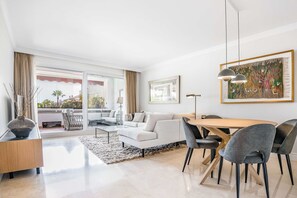 Un salon moderne avec un canapé blanc, une table à manger et des chaises, une grande fenêtre avec des rideaux et un tableau accroché au mur.