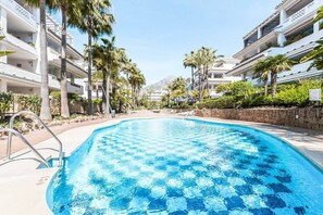 Ein Swimmingpool mit Schachbrettmuster, umgeben von Palmen und mehrstöckigen Gebäuden.