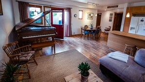 Una sala de estar con un piano de cola, un sofá, un comedor con mesa y sillas, y una cocina con armarios de madera.