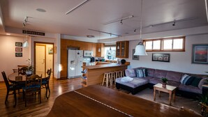 Una cocina moderna con armarios de madera, una isla central y taburetes de bar. Se ve un rincón comedor con una mesa y sillas de madera.