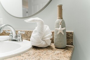 A bathroom sink with a granite countertop, a white towel, and a decorative bottle with a starfish. - Enjoy our beachfront property! (North Myrtle Beach)