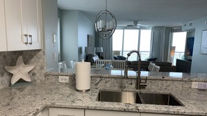 Una cocina moderna con encimeras de granito, armarios blancos y un lavamanos de acero inoxidable.