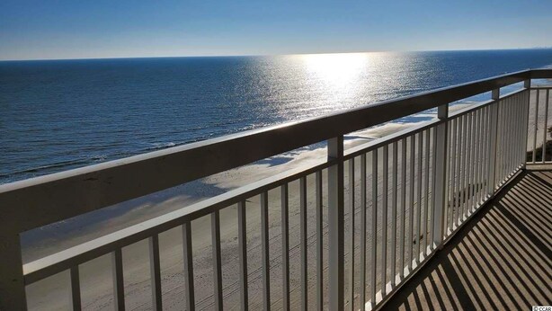 Una terraza de madera con barandilla que da a una playa.