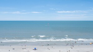 Una playa con gente, un paracaídas y un cielo despejado.