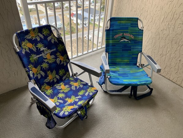 Two beach chairs with tropical patterns, one with a pineapple design and the other with a blue and green pattern, on a balcony with a view of a residential area. - Enjoy our beachfront property! (North Myrtle Beach)