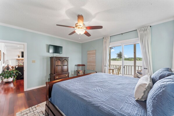A bedroom with a large bed, a ceiling fan, a TV, a wooden dresser, a chair, and a view of the outdoors through a window. - Lay Lake - On main Channel in private area. With Hot Tub and Kayaks (Wilsonville)