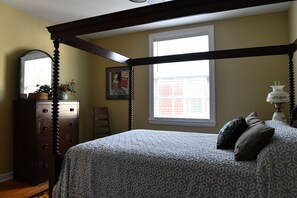 Classic bedroom with a four-poster bed, wooden dresser, and mirror.