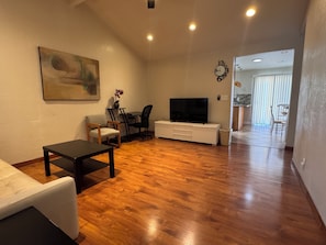 A living room with a TV, sofa, chairs, and a painting on the wall.
