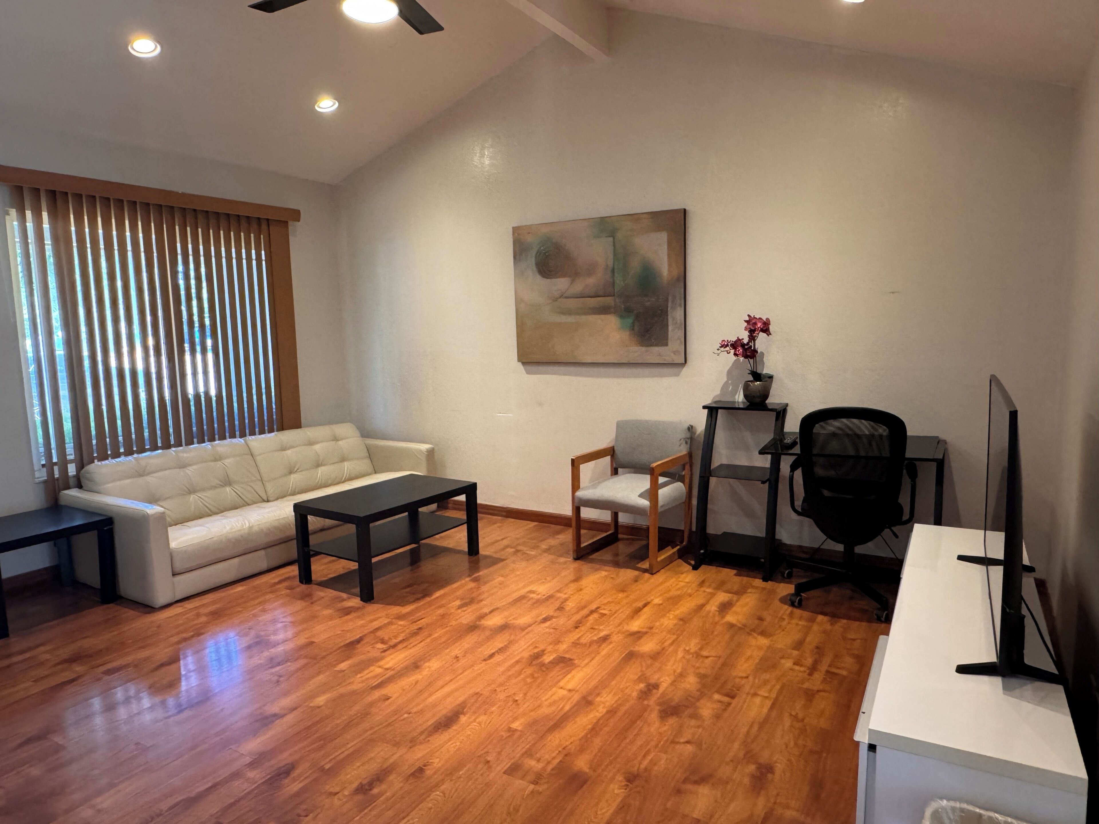 A living room with a sofa, a coffee table, a chair, a desk with a computer, and a painting on the wall.