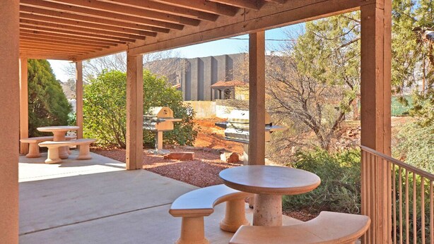 Un patio al aire libre con mesas y bancos de terracota, una pérgola en la parte superior y vistas a un paisaje montañoso.
