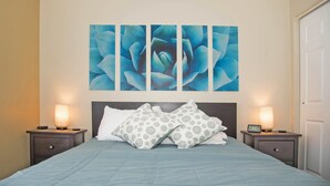 Un dormitorio con una cama, dos mesitas de noche, un reloj de pared y un cuadro grande con motivos florales.