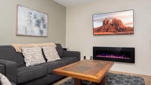 Una sala de estar con un sofá, una mesa de centro, una chimenea y dos televisores empotrados mostrando diferentes escenas.