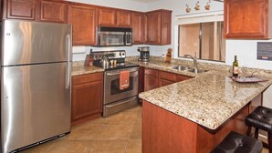 Una cocina con gabinetes de madera, electrodomésticos de acero inoxidable, encimera de granito y una isla integrada con taburetes.