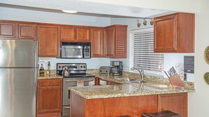 Una cocina con armarios de madera, un refrigerador de acero inoxidable, un microondas, una estufa y una encimera de granito.