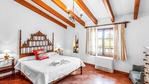 A bedroom with a wooden bed frame, a large window with curtains, a chandelier, and a radiator. - REI PETIT.  Splendidly maintained garden for a perfect experience (Pollensa)