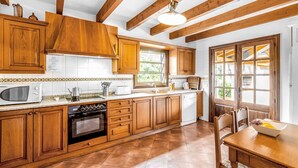 A kitchen with wooden cabinets, a stove, a microwave, and a window with a view of greenery. - REI PETIT.  Splendidly maintained garden for a perfect experience (Pollensa)