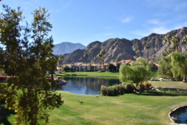 A golf course with a pond, trees, and mountains in the background.