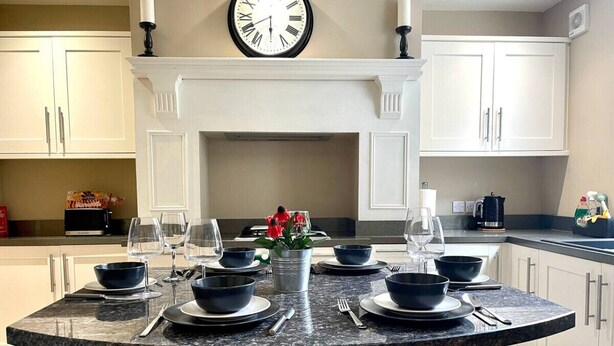 Une cuisine moderne avec des meubles blancs, un îlot en granit aménagé en coin repas et une horloge au mur.