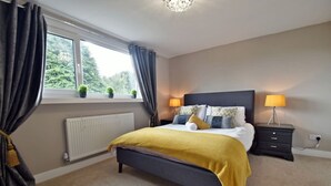 Une chambre à coucher comprenant un lit, des tables de chevet, une fenêtre avec des rideaux et un radiateur.