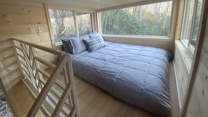 A bedroom with a bed, a window, and a wooden railing.