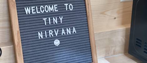 Ein gerahmtes Schild mit dem Aufschrift 'WELCOME TO TINY NIRVANA' vor einem strukturierten Hintergrund.