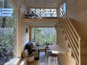 Ein Holzblockhaus-Innenraum mit Schlafzimmer im oberen Bereich, einem Essbereich und Blick auf den Wald.