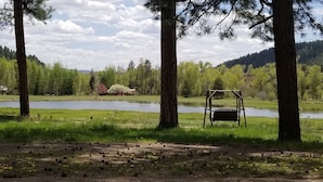 A serene outdoor setting with a pond, a wooden swing, and a bench.