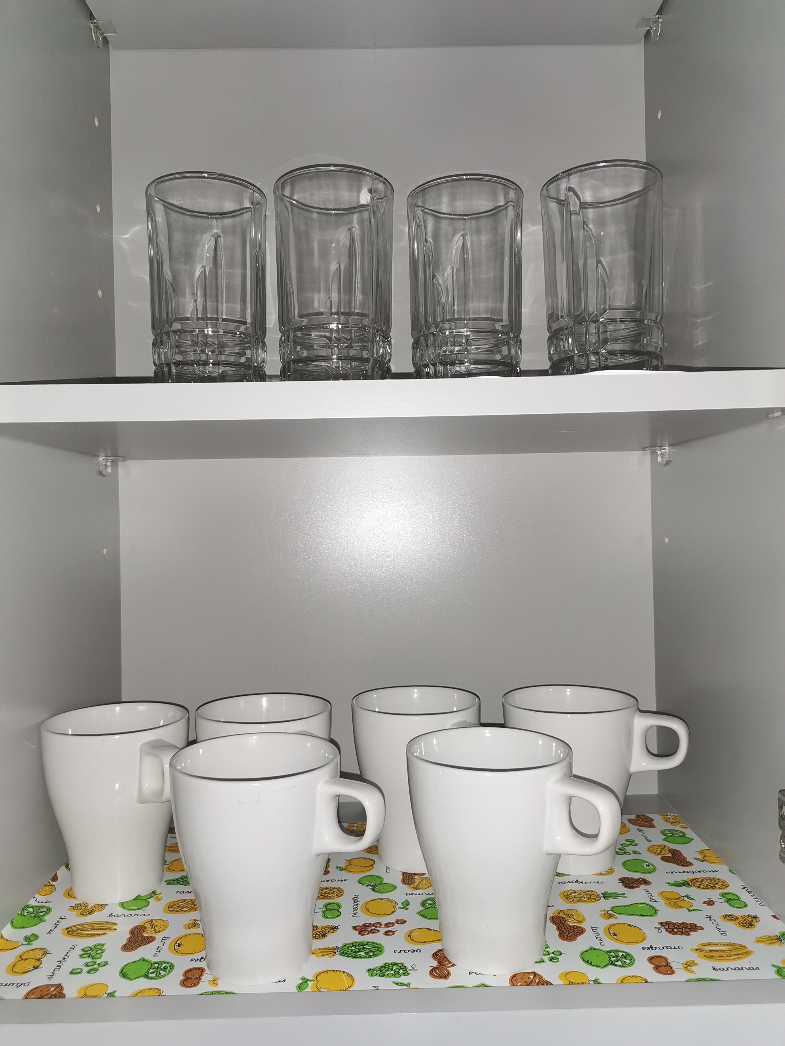 En hylde med fire glas og seks hvide krus med sort kant.