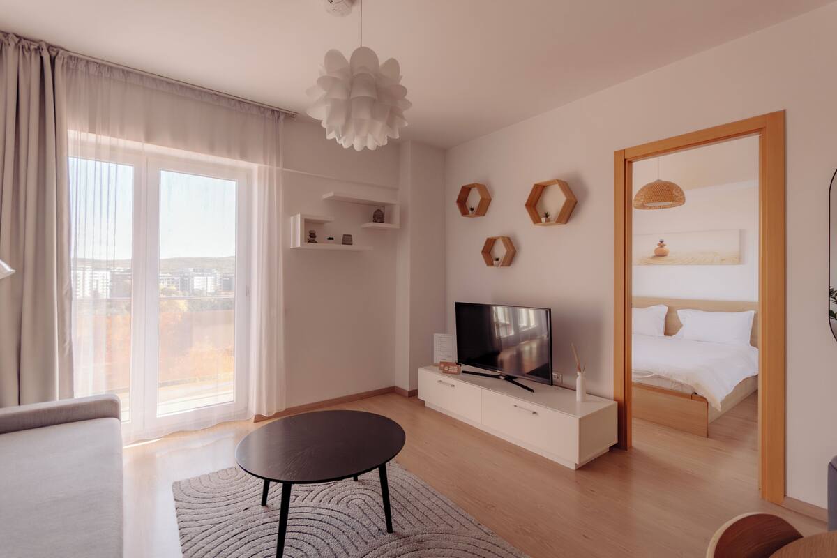 Uma sala de estar moderna com televisão de tela plana, sofá, mesa de centro e uma janela grande com cortinas.