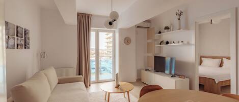 Una habitación de hotel moderna con sofá, mesa de comedor, televisor y cama.