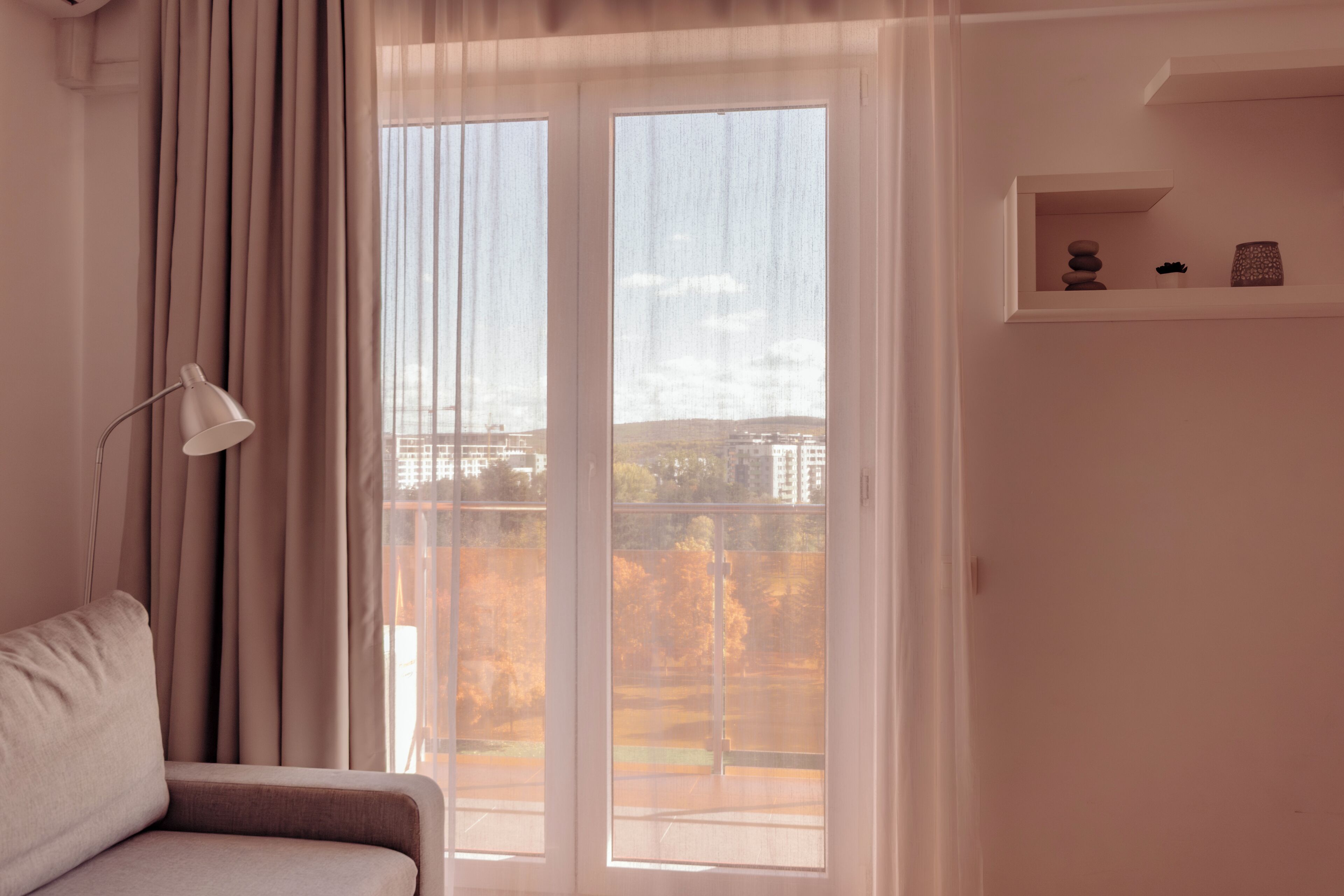 A room with a sofa, a lamp, a window with curtains, and a shelf with decorative items.