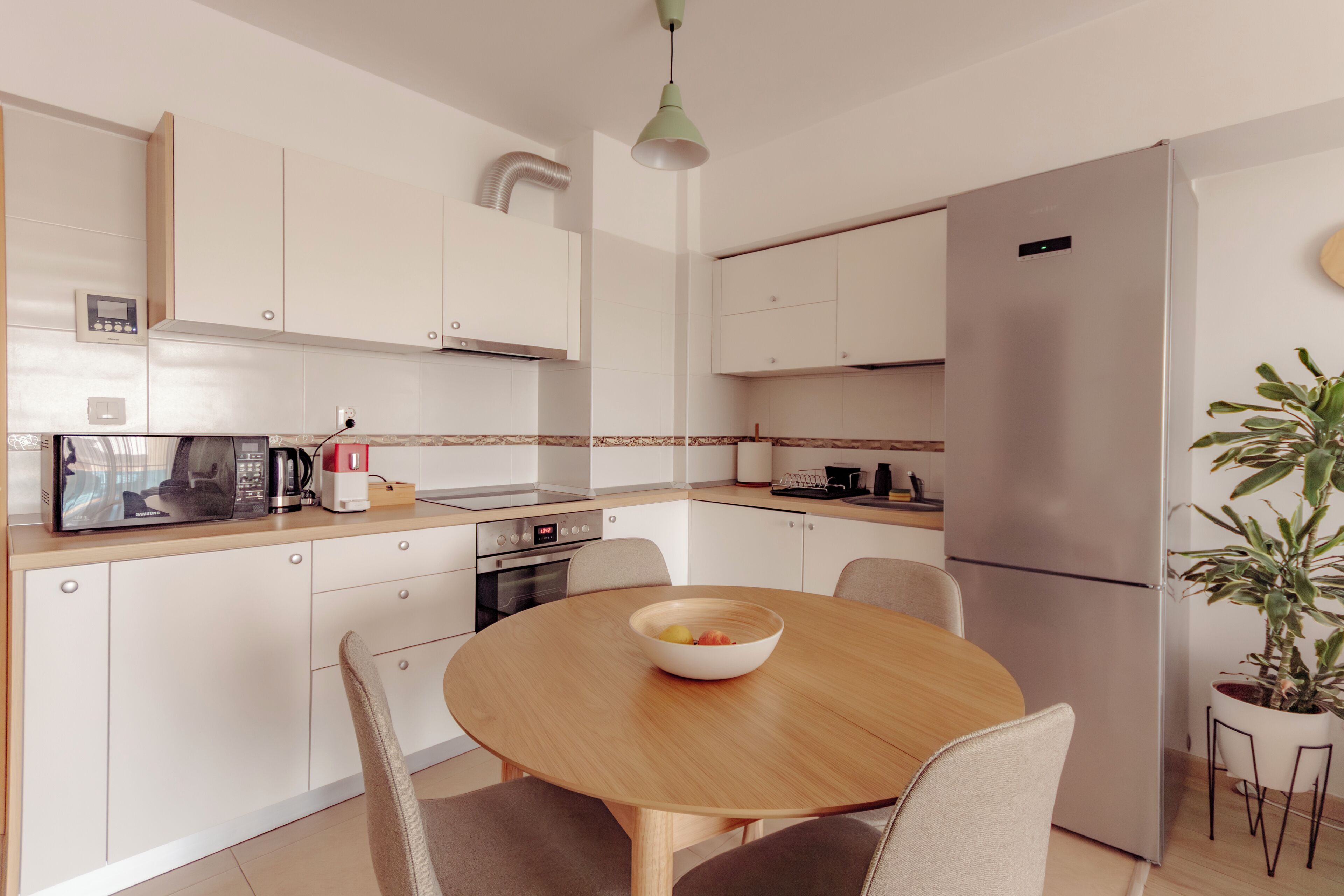 A modern kitchen with white cabinets, a stainless steel refrigerator, a microwave, and a dining table with chairs.