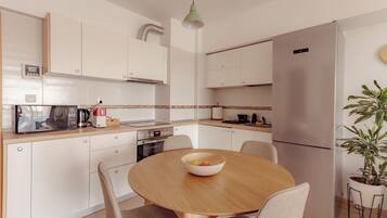 A modern kitchen with white cabinets, a stainless steel refrigerator, a microwave, and a dining table with chairs.