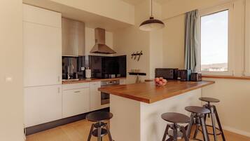 A modern kitchen with white cabinets, a wooden island, bar stools, and a large window.
