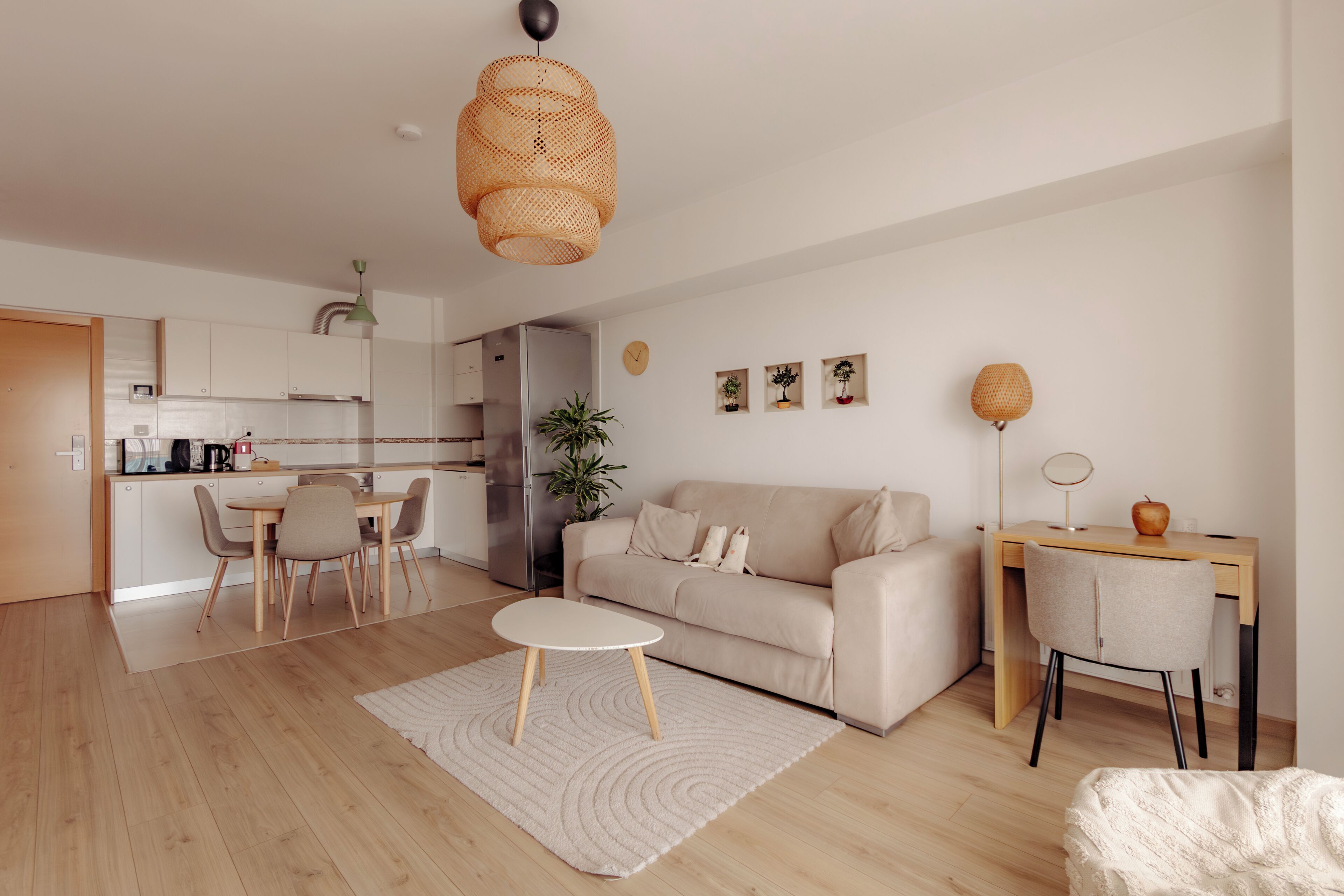 A modern living room with a sofa, dining table, and chairs, a kitchen in the background, and a large woven pendant light.