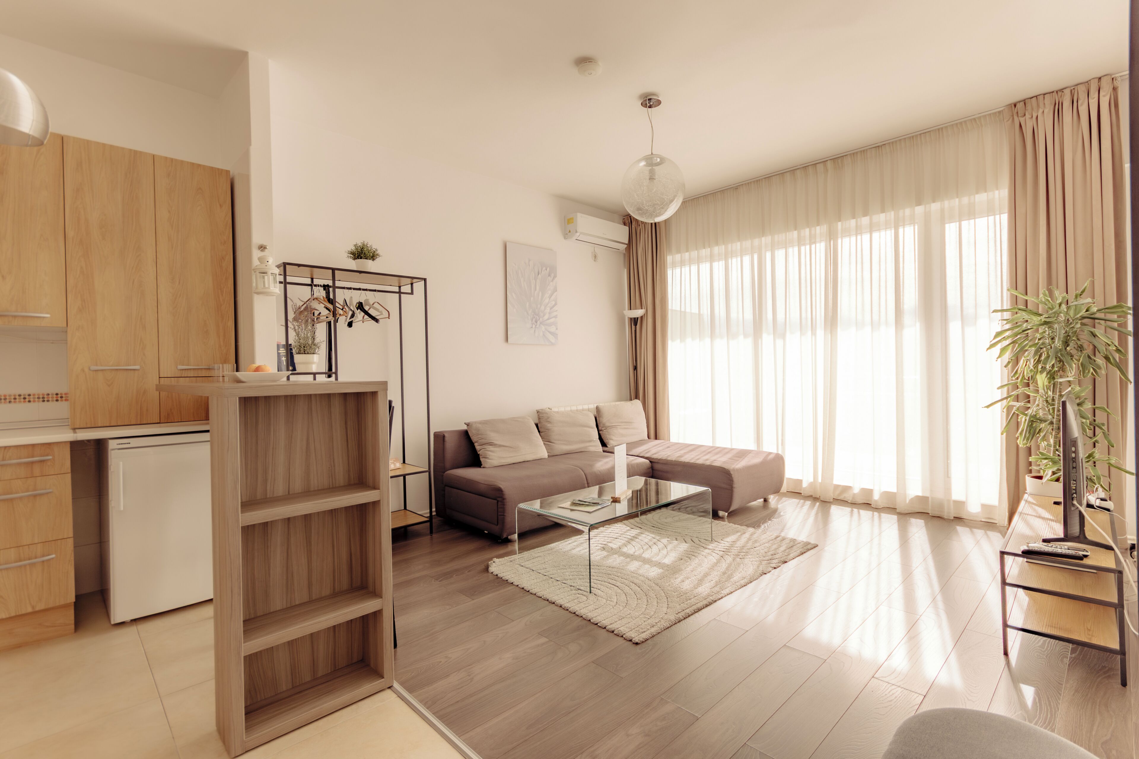 Una sala de estar moderna con un sofá, una mesa de centro y un comedor con un armario de madera y un refrigerador pequeño.