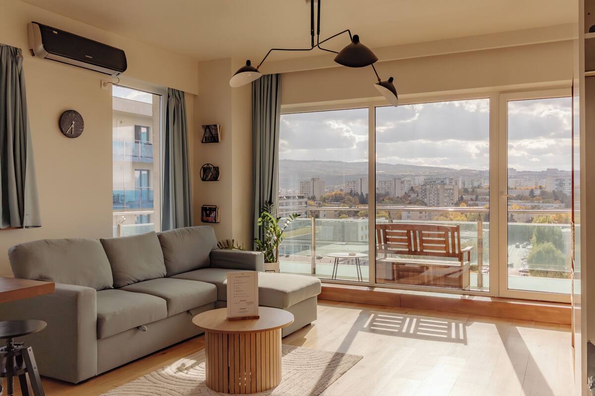 Sala de estar moderna com sofá, mesa de centro e varanda com vista para a cidade.